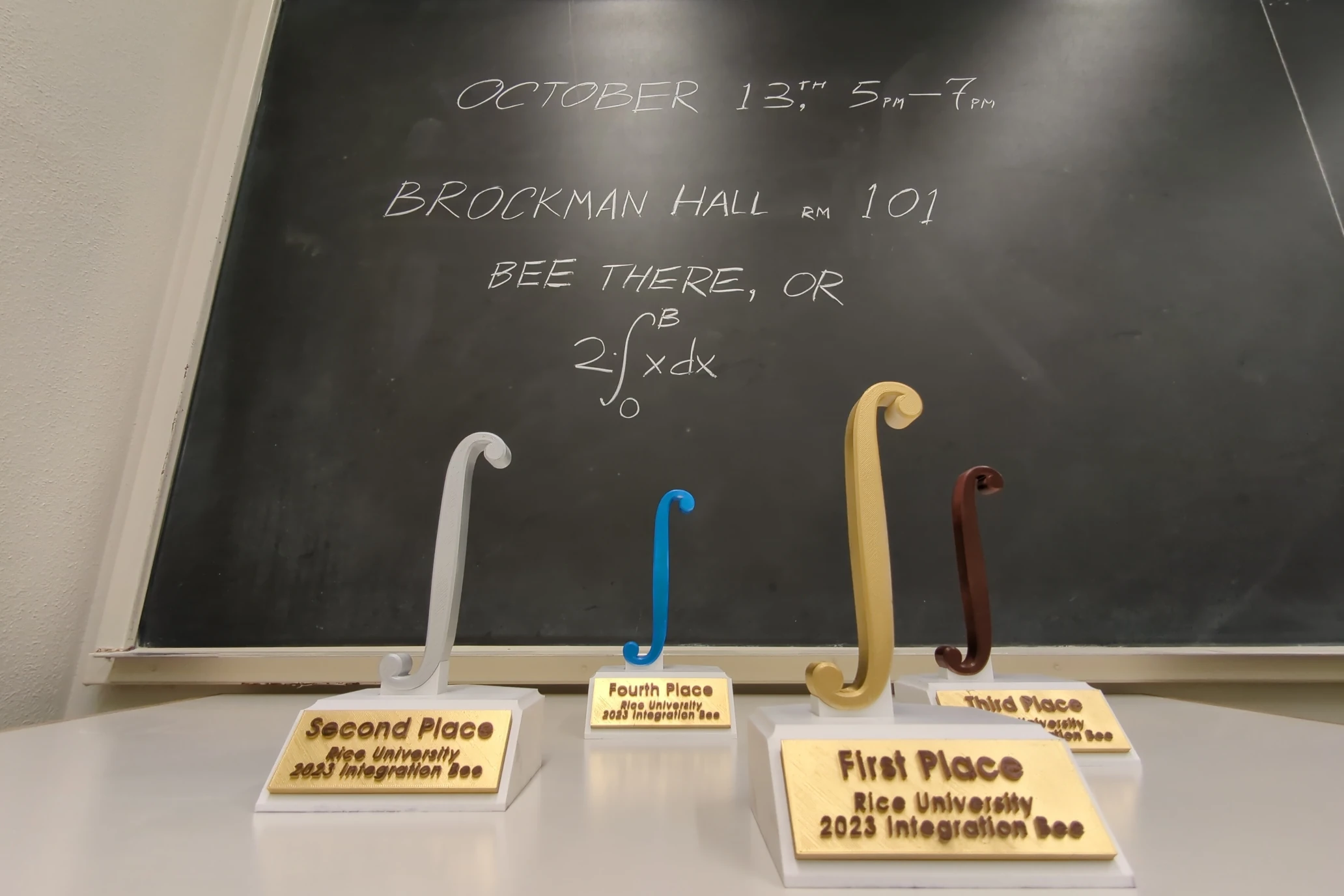 Teaser advertisement. 3D-printed integral-shaped trophies. Bee there, or twice the integral of x from 0 to B.